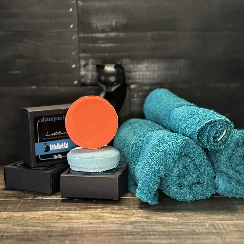 an artistically arranged product photo of lotion bottles with a towel and a little cup of lotion displayed